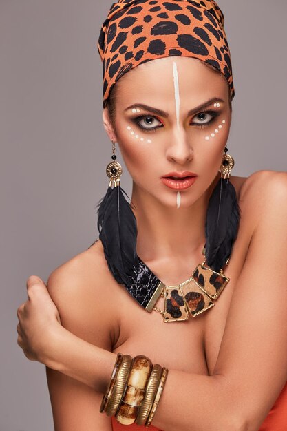 Concetto di moda. Bella donna caucasica con trucco che indossa uno scialle colorato sulla testa e accessori. Isolato su sfondo grigio.