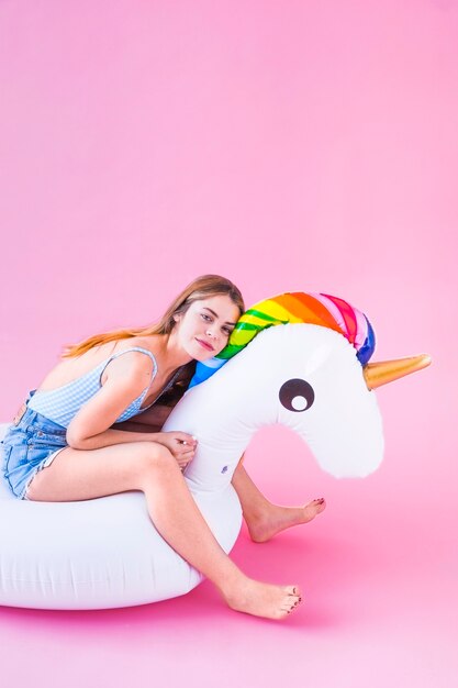 Concetto di moda di estate con la giovane donna sull'unicorno gonfiabile