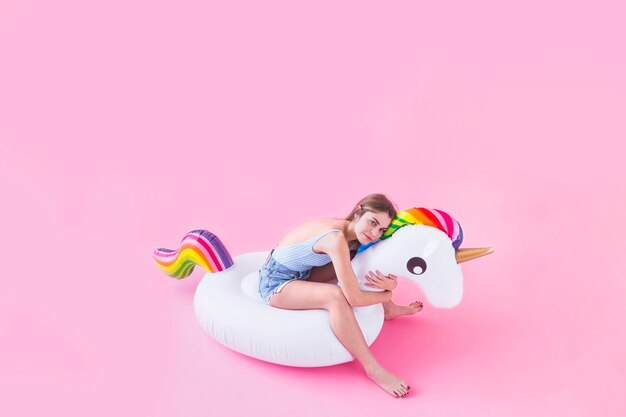 Concetto di moda di estate con la giovane donna sull'unicorno gonfiabile
