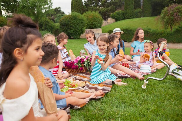 Concetto di moda per bambini. gruppo di ragazze adolescenti seduto all'erba verde al parco