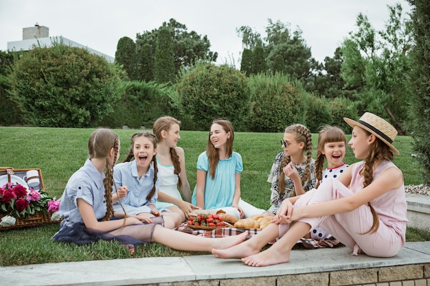 Concetto di moda per bambini. Il gruppo di ragazze teenager che si siedono all'erba verde al parco