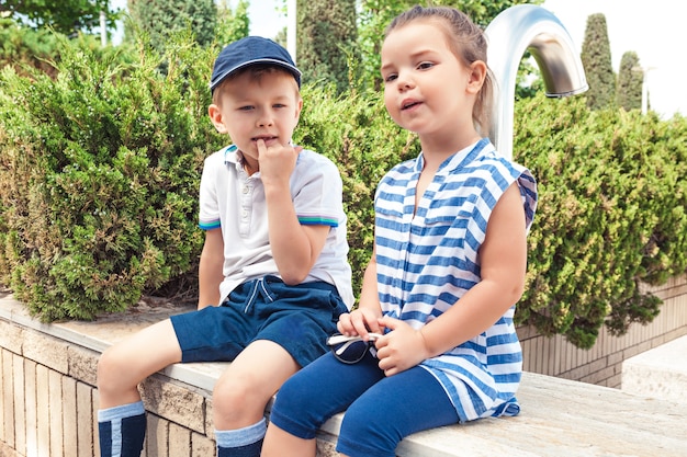 Concetto di moda per bambini. Il ragazzo e la ragazza teenager che si siedono al parco.