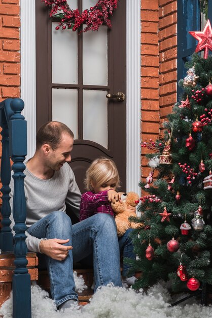 Concetto di Natale con il papà e la figlia che si siedono davanti alla porta