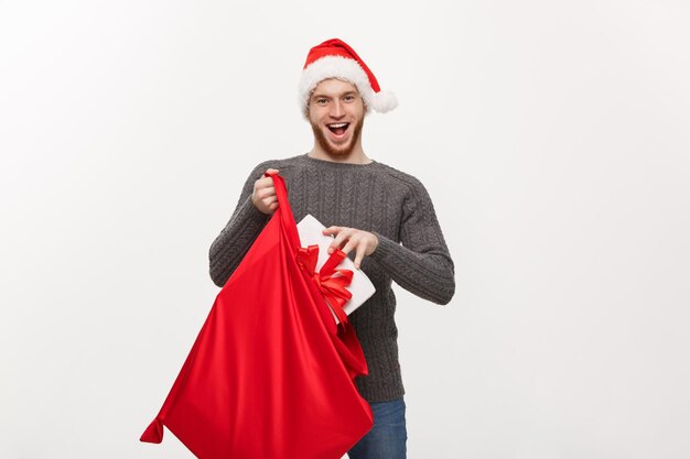 Concetto di Natale Il giovane uomo con la barba felice si eccita con un grande regalo nella borsa di Babbo Natale