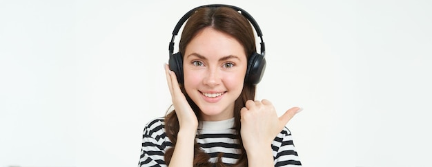 Concetto di negozio di musica giovane donna sorridente che ascolta una canzone con le cuffie che punta a sinistra nello spazio di copia