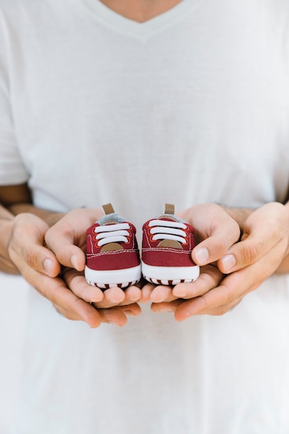 Concetto di neonato con i genitori mani che tengono le scarpe