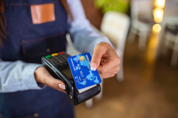 Concetto di pagamento senza contatto femmina che tiene la carta di credito vicino alla tecnologia NFC sul contatore client effettua la transazione pagare la fattura sul terminale rfid cassiere nel negozio ristorante vista ravvicinata