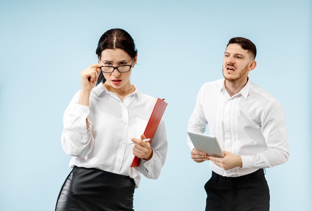 Concetto di partnership nel mondo degli affari. Giovane uomo emotivo e donna su sfondo blu in studio. Le emozioni umane e il concetto di partnership