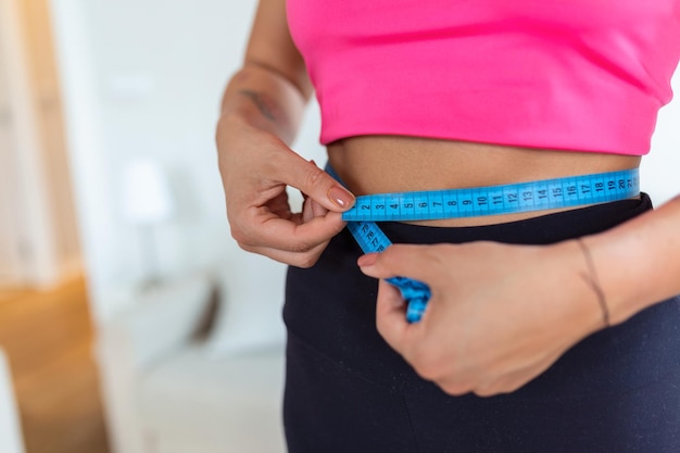 Concetto di perdita di peso Ritratto di una donna afroamericana millenaria con reggiseno e leggings che si misurano la vita utilizzando nastro blu spazio di copia gratuito Donna nera che controlla i parametri del corpo