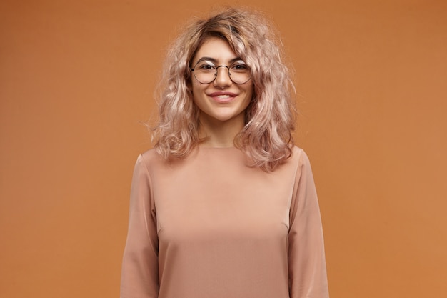 Concetto di persone, stile di vita, moda e ottica. Attraente ragazza europea adorabile hipster con capelli voluminosi e sorriso amichevole allegro che esprime emozioni positive