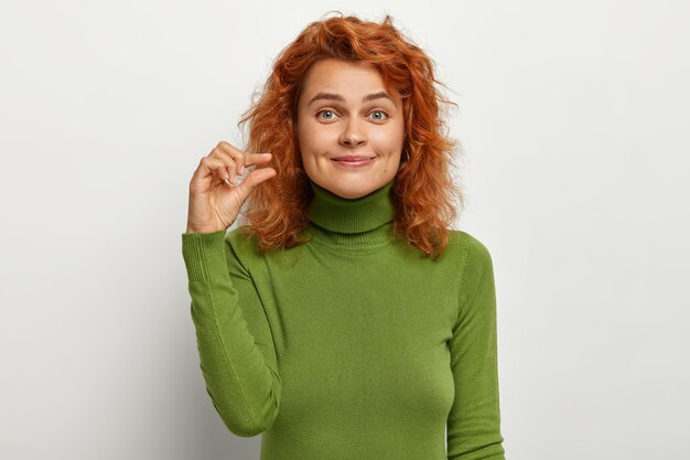 Concetto di piccole dimensioni. La bella giovane femmina dai capelli rossi lieta modella qualcosa di piccolo