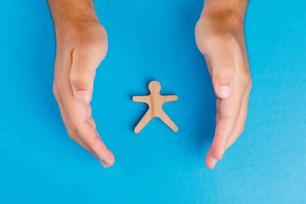 Concetto di protezione sociale sulla disposizione blu del piano della tavola. mani prendendosi cura della figura umana in legno.