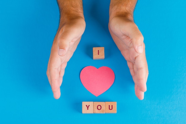 Concetto di relazione con i cubi di legno sulla disposizione blu del piano della tavola. mani che proteggono la carta tagliata a cuore.