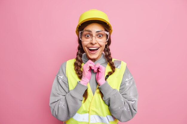 Concetto di riparazione. Il meccanico positivo della donna indossa l'uniforme dell'edificio di ingegneria sembra felicemente isolato sul muro rosa. Ingegneria ed edilizia industriale. Operaio in abiti da lavoro