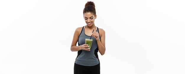 Concetto di salute e fitness Bella signora africana americana in abbigliamento fitness che beve una bevanda vegetale sana isolata su sfondo bianco