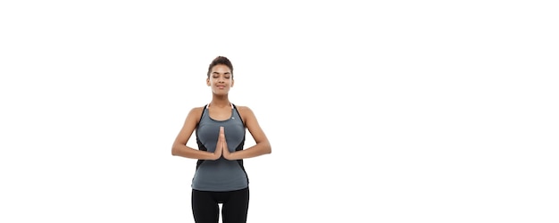 Concetto di salute e fitness Bella signora africana americana in abbigliamento fitness facendo yoga e meditazione isolata su sfondo bianco