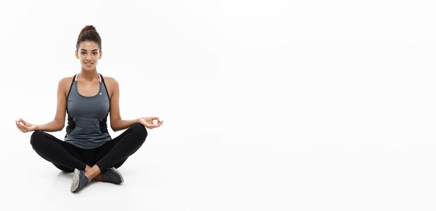 Concetto di salute e fitness Bella signora africana americana in abbigliamento fitness facendo yoga e meditazione isolata su sfondo bianco