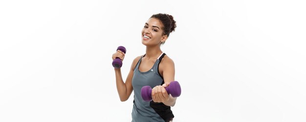 Concetto di salute e fitness Bella signora africana americana in abiti fitness allenamento con manubrio isolato su sfondo bianco