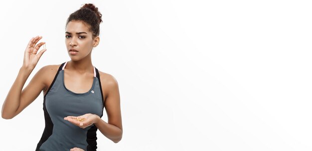 Concetto di salute e fitness Closeup ritratto di bella afroamericana prendendo una pillola di olio di fegato di merluzzo isolato su sfondo bianco per studio