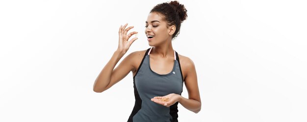 Concetto di salute e fitness Closeup ritratto di bella afroamericana prendendo una pillola di olio di fegato di merluzzo isolato su sfondo bianco per studio