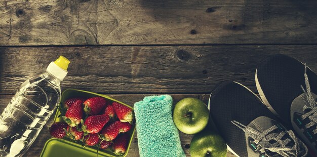 Concetto di salute sano della vita. Sneakers con mele, asciugamano e bottiglia di acqua su sfondo in legno. Spazio di copia.