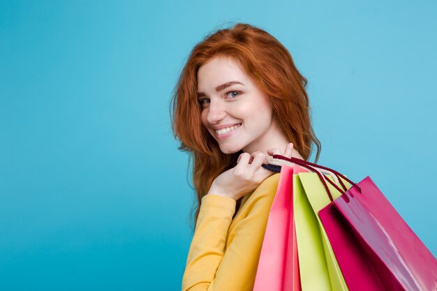 Concetto di shopping - Close up Ritratto di giovane bella ragazza attraente redhair sorridente guardando la fotocamera con borsa della spesa. Sfondo blu pastello. Copia spazio.