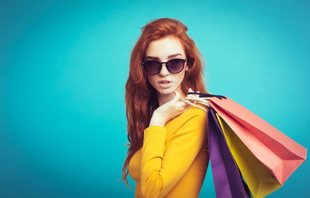 Concetto di shopping - Close up Ritratto di giovane bella ragazza attraente redhair sorridente guardando la fotocamera con borsa della spesa. Sfondo blu pastello. Copia spazio.