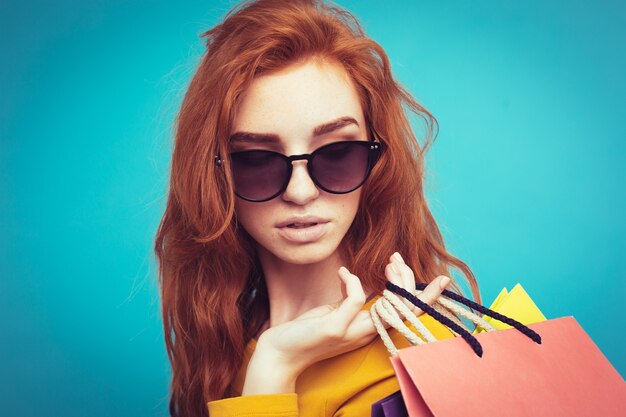 Concetto di shopping - Close up Ritratto di giovane bella ragazza attraente redhair sorridente guardando la fotocamera con borsa della spesa. Sfondo blu pastello. Copia spazio.