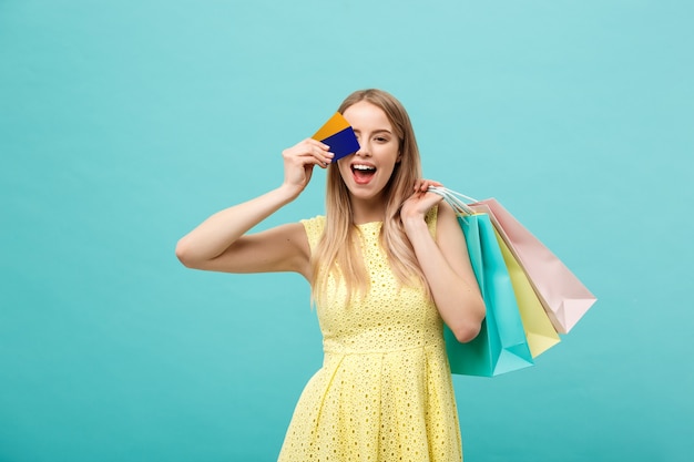 Concetto di shopping e stile di vita: bella ragazza con carta di credito e borse della spesa colorate. Isolato su sfondo blu.