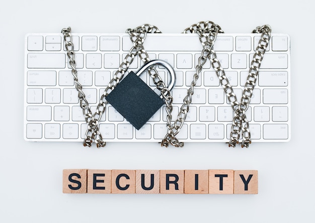 Concetto di sicurezza informatica con catena e lucchetto sulla tastiera, cubi in legno su sfondo bianco piano laici.