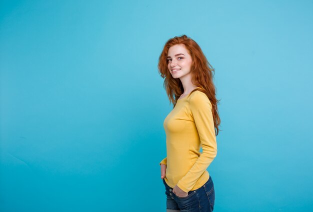 Concetto di stile di vita - Close up Ritratto di giovane bella ragazza attraente di zenzero rosso capelli che giocano con i capelli con timidezza. Sfondo blu pastello. Copia spazio.