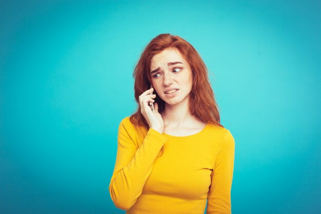 Concetto di stile di vita - Ritratto di ragazza di capelli rossi zenzero con espressione scioccante e stressante mentre parla con l&#39;amico dal telefono cellulare. Isolato su sfondo blu pastello. Copia spazio.