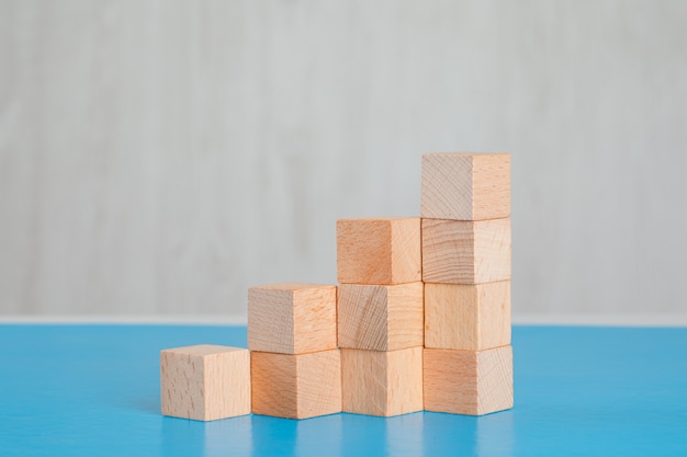 Concetto di successo di affari con la pila di cubi di legno sulla vista laterale della tavola blu e grigia.