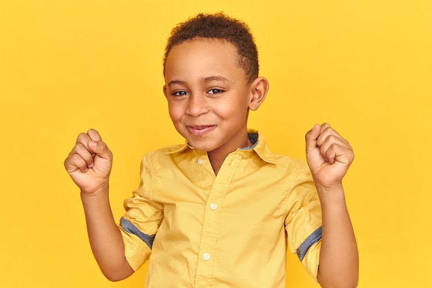 Concetto di successo, trionfo, gioia e felicità. Adorabile carino eccitato ragazzino afroamericano con un'espressione facciale estatica felicissima, sorridente, pugni serrati, ricezione di buone notizie positive