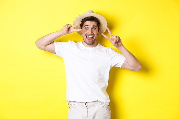 Concetto di turismo e vacanza. Turista dell'uomo felice in posa per una foto con segni di pace, sorridente eccitato, in piedi su sfondo giallo.