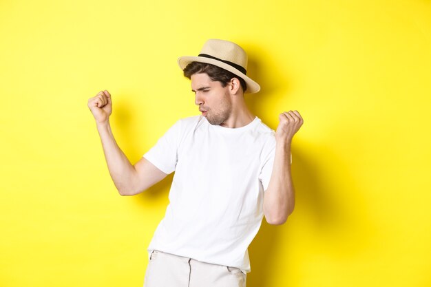 Concetto di turismo e vacanze. Turista del ragazzo fortunato che si rallegra, facendo la pompa del pugno e dicendo di sì, in piedi contento su sfondo giallo.