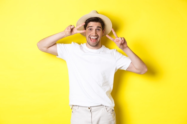 Concetto di turismo e vacanze. Turista uomo felice in posa per una foto con segni di pace, sorridendo eccitato, in piedi su sfondo giallo.