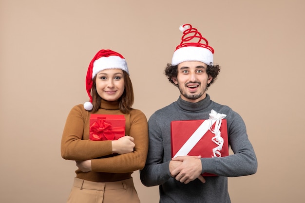 Concetto di umore e festa del nuovo anno - giovani coppie adorabili eccitate che indossano cappelli di Babbo Natale su grigio