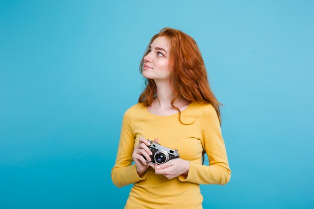 Concetto di viaggio - Close up Ritratto di giovane bella ragazza attraente redhair con cappello alla moda, sunglass e macchina fotografica d&#39;epoca sorridente alla fotocamera. Sfondo blu pastello. Copia spazio.