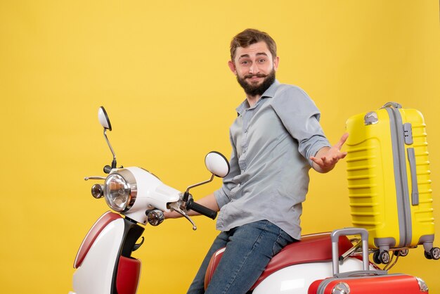 Concetto di viaggio con curioso giovane uomo seduto sulla moto con le valigie su di esso su giallo