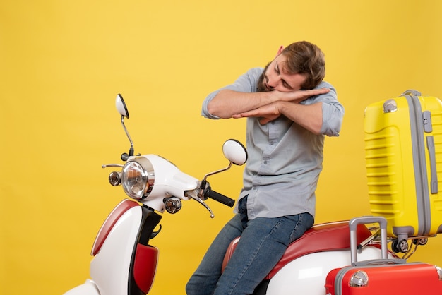 Concetto di viaggio con il giovane uomo barbuto assonnato seduto sulla moto su di esso su giallo