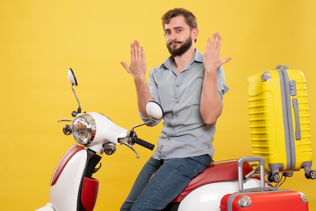 Concetto di viaggio con il giovane uomo barbuto emotivo seduto sulla moto su di esso che mostra le mani sul giallo