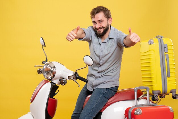 Concetto di viaggio con il giovane uomo barbuto felice sorridente che si siede sulla motocicletta e che fa il gesto giusto su di esso su colore giallo