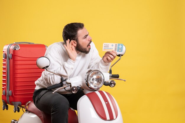 Concetto di viaggio con il giovane uomo seduto sulla moto con la valigia su di esso che mostra il biglietto e ascolta l'ultimo spettegolare sul giallo