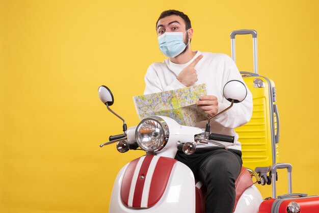 Concetto di viaggio con ragazzo sorpreso in maschera medica seduto su moto con valigia gialla su di esso