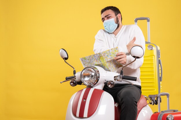 Concetto di viaggio con un giovane ragazzo in maschera medica seduto su una moto con una valigia gialla sopra