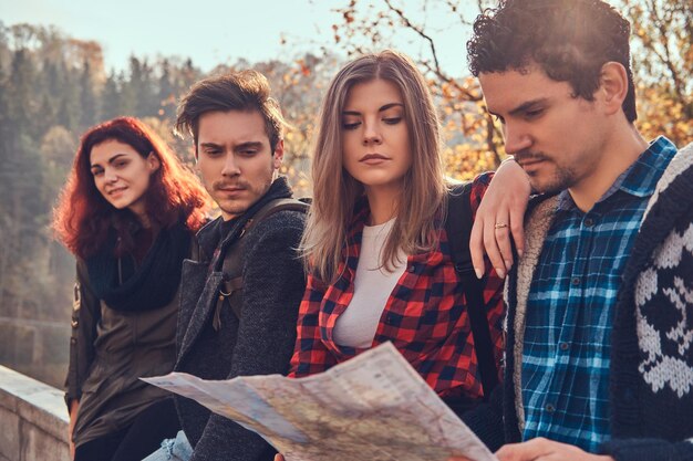 Concetto di viaggio, turismo, escursione e persone. Foto ravvicinata di giovani amici che guardano la mappa e pianificano il viaggio nella foresta autunnale.