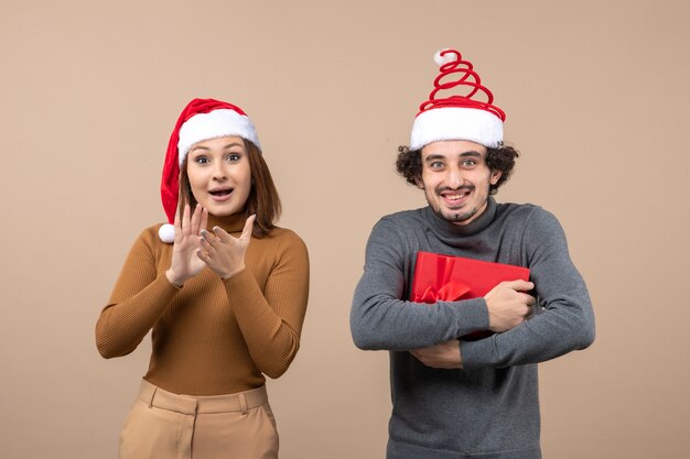 Concetto festivo di umore del nuovo anno con le coppie adorabili felici divertenti che portano i cappelli rossi del Babbo Natale su gray