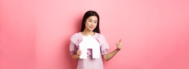 Concetto immobiliare e assicurativo bella donna asiatica che punta al ritaglio della casa di carta che mostra agenc