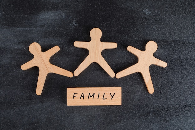 Concetto "nucleo familiare" con il blocco di legno e figure umane sulla disposizione piana del tavolo grigio scuro.